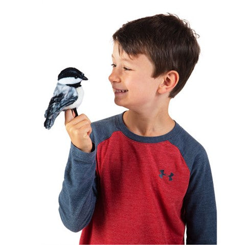 A young boy wearing a red and blue shirt plays with the Chickadee Finger Puppet on his finger.