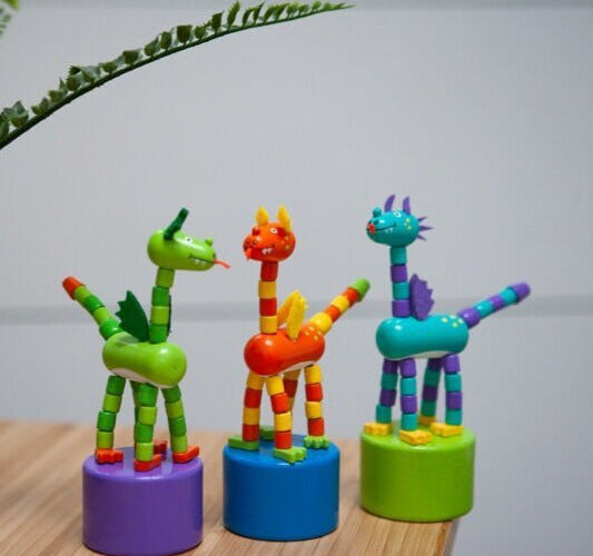 Three colorful ThumbToy Dragon push puppets standing on round bases, ready to droop and pop back up.