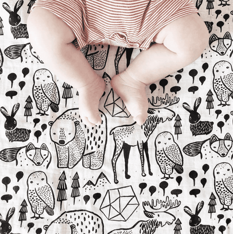 Organic Muslin Swaddle | Nordic featuring baby legs on a black and white animal-patterned organic cotton muslin fabric.