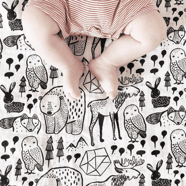 Organic Muslin Swaddle | Nordic featuring baby legs on a black and white animal-patterned organic cotton muslin fabric.