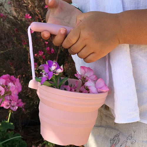 Child holding a pink Seedling Pot Rose filled with flowers, featuring a soft silicone collapsible design and rope handle.