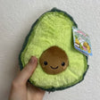 Hand holding a 5-inch soft and squishy avocado plush with embroidered smiling pit, Avocado Snackers.