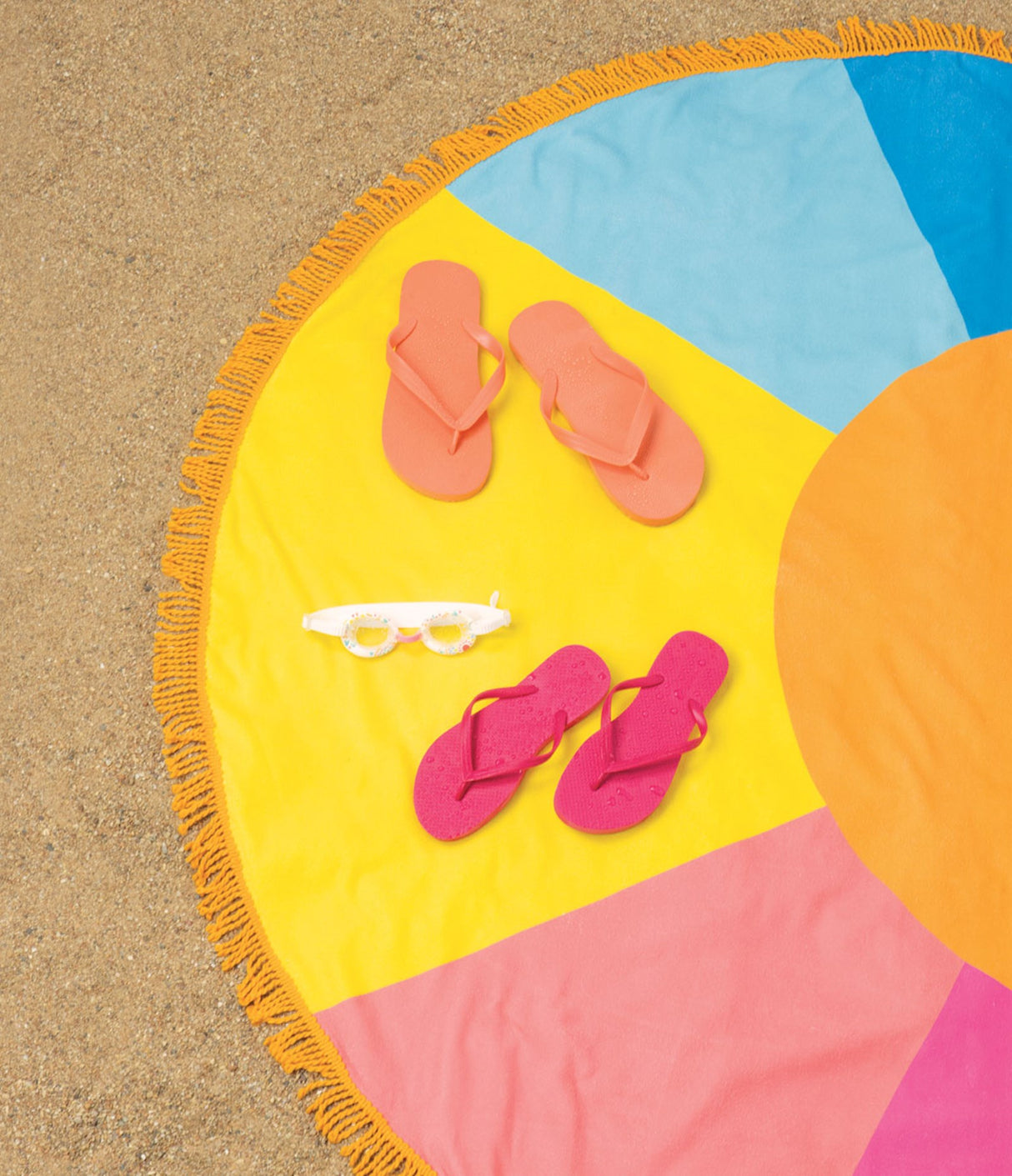 Round Beach Towel Here Comes the Sun on sand with colorful design, hand-dyed fringe, and summer essentials placed on it