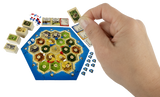 Hand holding a mini resource card over a compact, travel-sized Catan board game set up for play.