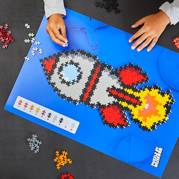Child assembling Plus Plus Puzzle by Number | Rocket with colorful pieces on a blue pattern board.