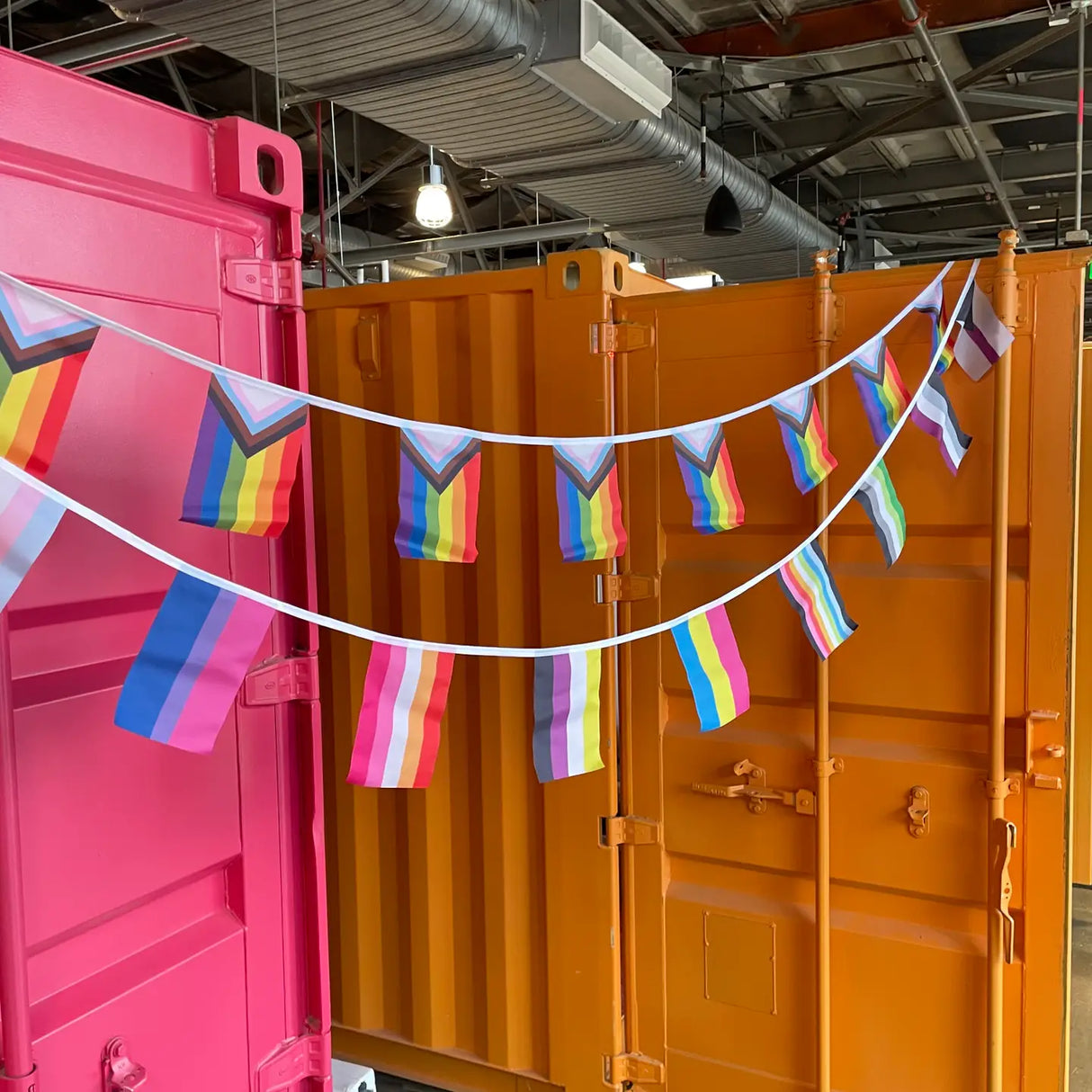Pride Flag Bunting with 12 colorful pride flags strung between vibrant pink and orange containers, perfect for decor or parties.