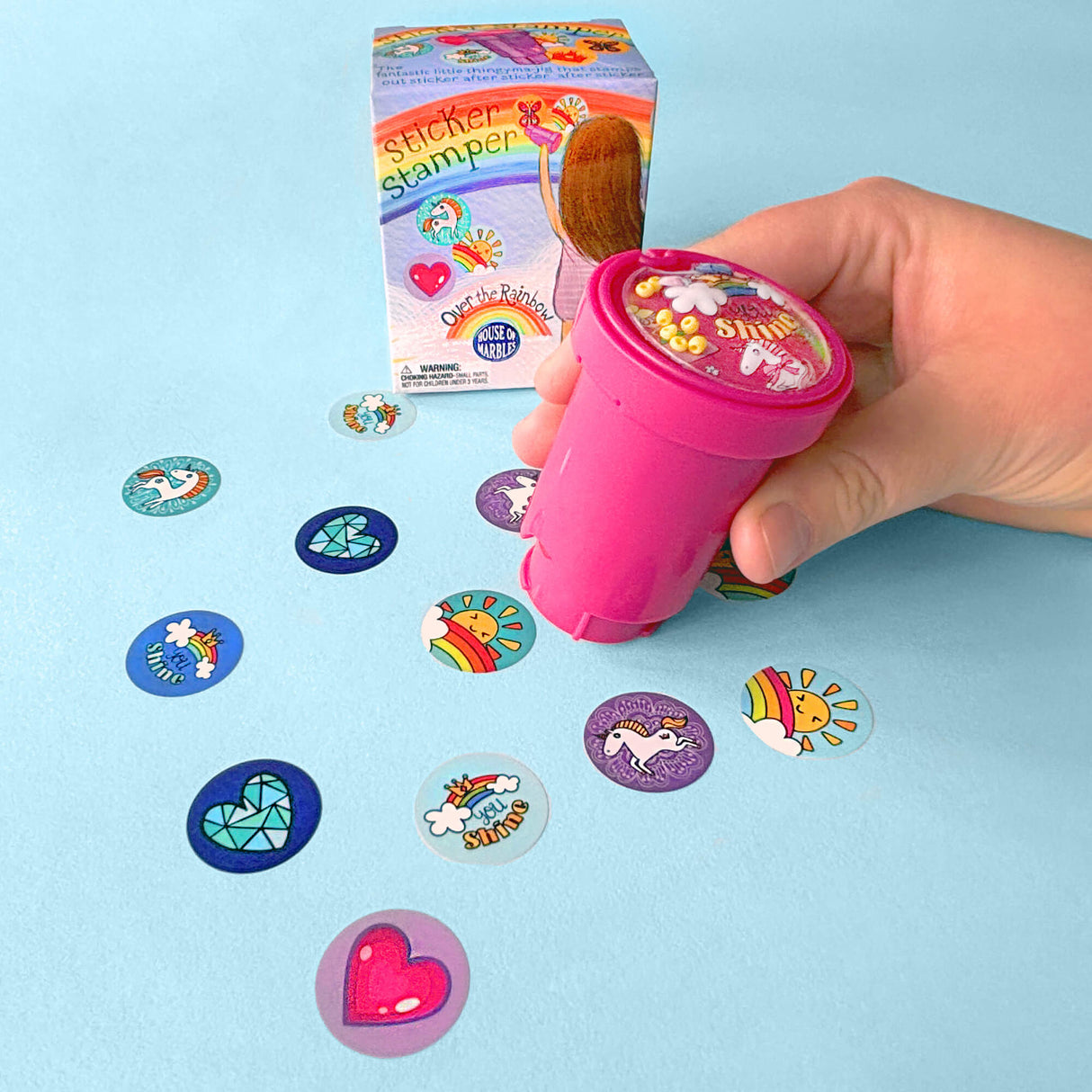 Depiction of child using the rainbow sticker stamper on a sheet of paper. For ages 3 and up.