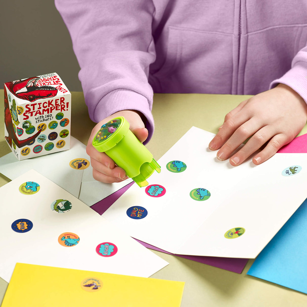 Depiction of child using the dinosaur sticker stamper on a sheet of paper. For ages 3 and up.