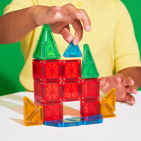 Child building colorful geometric shapes with Magnatiles Micromags Travel Set small magnetic tiles on table