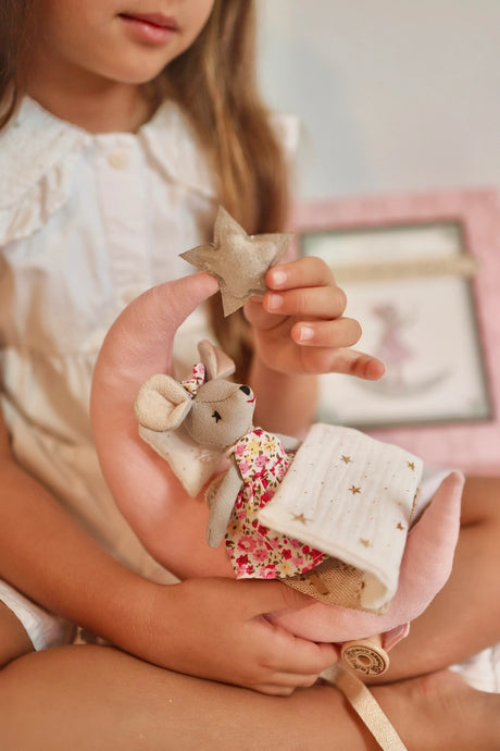 Child holding a soft toy mouse in a crescent moon bed with a star pillow and a floral dress