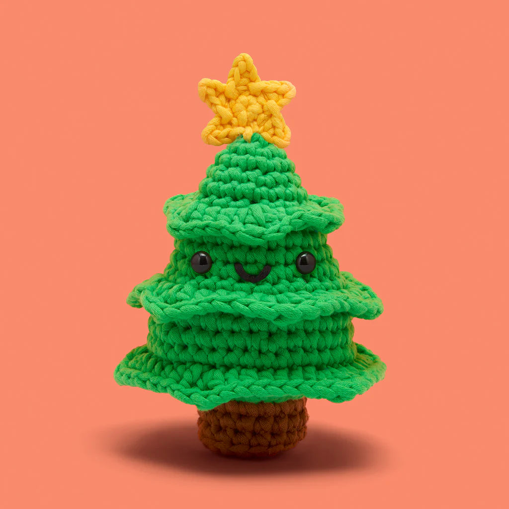 Crocheted green Christmas tree with smiling face and yellow star on top on an orange background