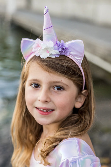 A smiling girl wearing the Alicorn Dress & Wings & Headband with iridescent unicorn horn and floral decorations.