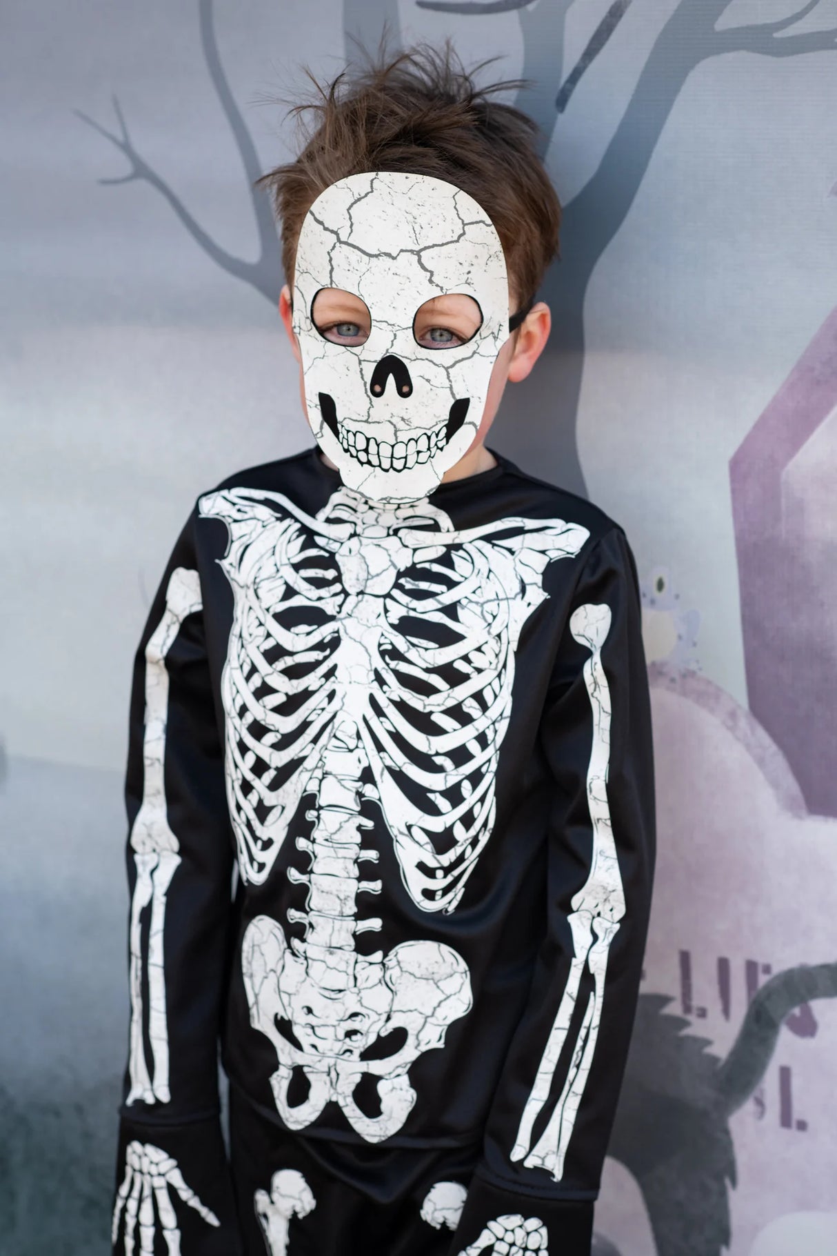 Child wearing Skeleton Outfit | Size 5-6 with detailed skeleton print and matching skull mask against a Halloween backdrop.