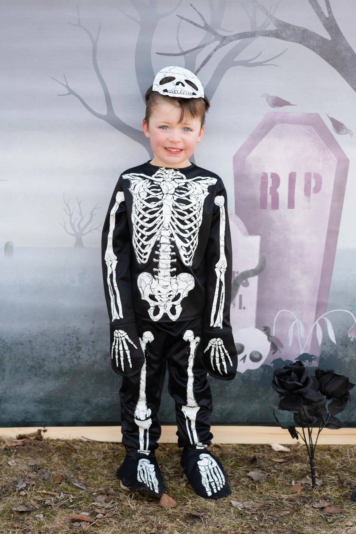 Skeleton Outfit | Size 5-6 worn by child in front of tombstone backdrop with skeleton mask on head.