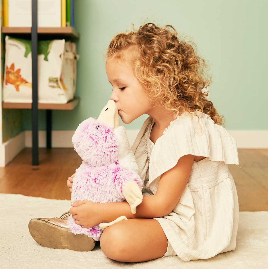 Young child sitting indoors cuddling and kissing a soft plush platypus warming toy scented with lavender