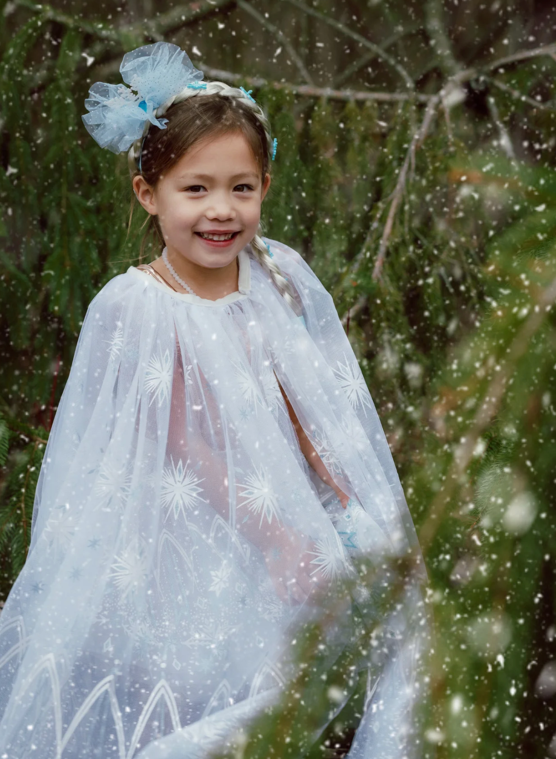 Winter Wonderland Cape | Size 3-4 worn by smiling child with icy white tulle and snowflake designs in snowy forest background.