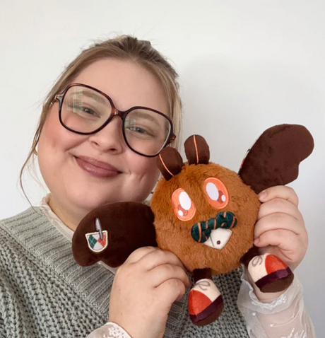 Woman holding the plush toy Alter Ego | Professor Baby Mothman with a friendly smile and glasses