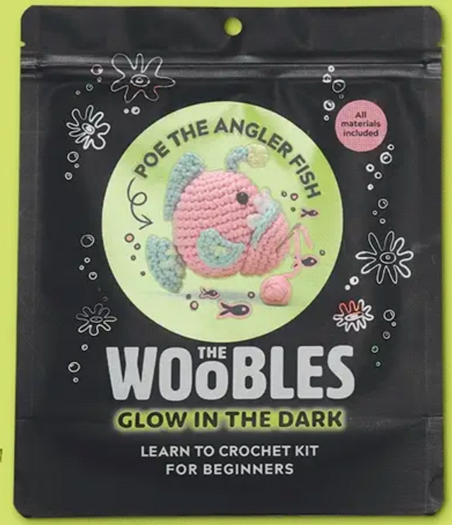 Poe the Angler Fish crochet kit packaging showing a pink and blue crocheted fish with glow in the dark yarn included.
