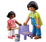 Two figures painting a small wooden chair purple with paint and brush, surrounded by paint accessories