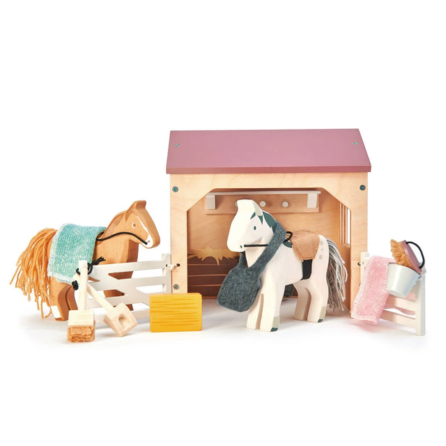 The Stables wooden playset with two ponies, grooming brush, blankets, hay bale, and stable accessories for kids.