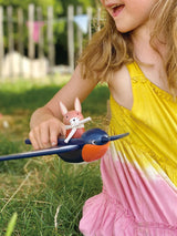 Child playing outdoors with Swifty Bird wooden toy featuring pilot Hare Spud with scarf on swallow's back.