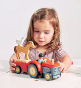Child playing with a bright red wooden Farmyard Tractor toy with driver, trailer, horse, and goose.