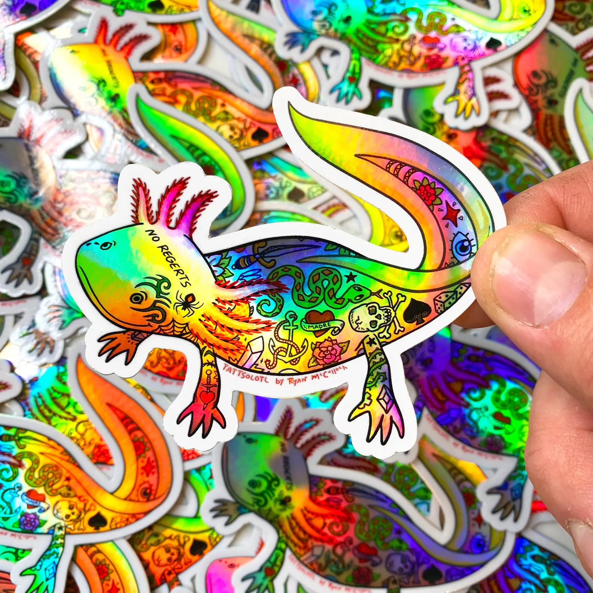 Tattsolotl Tattooed Axolotl Sticker with colorful, detailed tattoo designs on a holographic vinyl background held by hand.