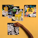 Child coloring black and white velvet animal sheets including camel and lion on yellow background with product box visible