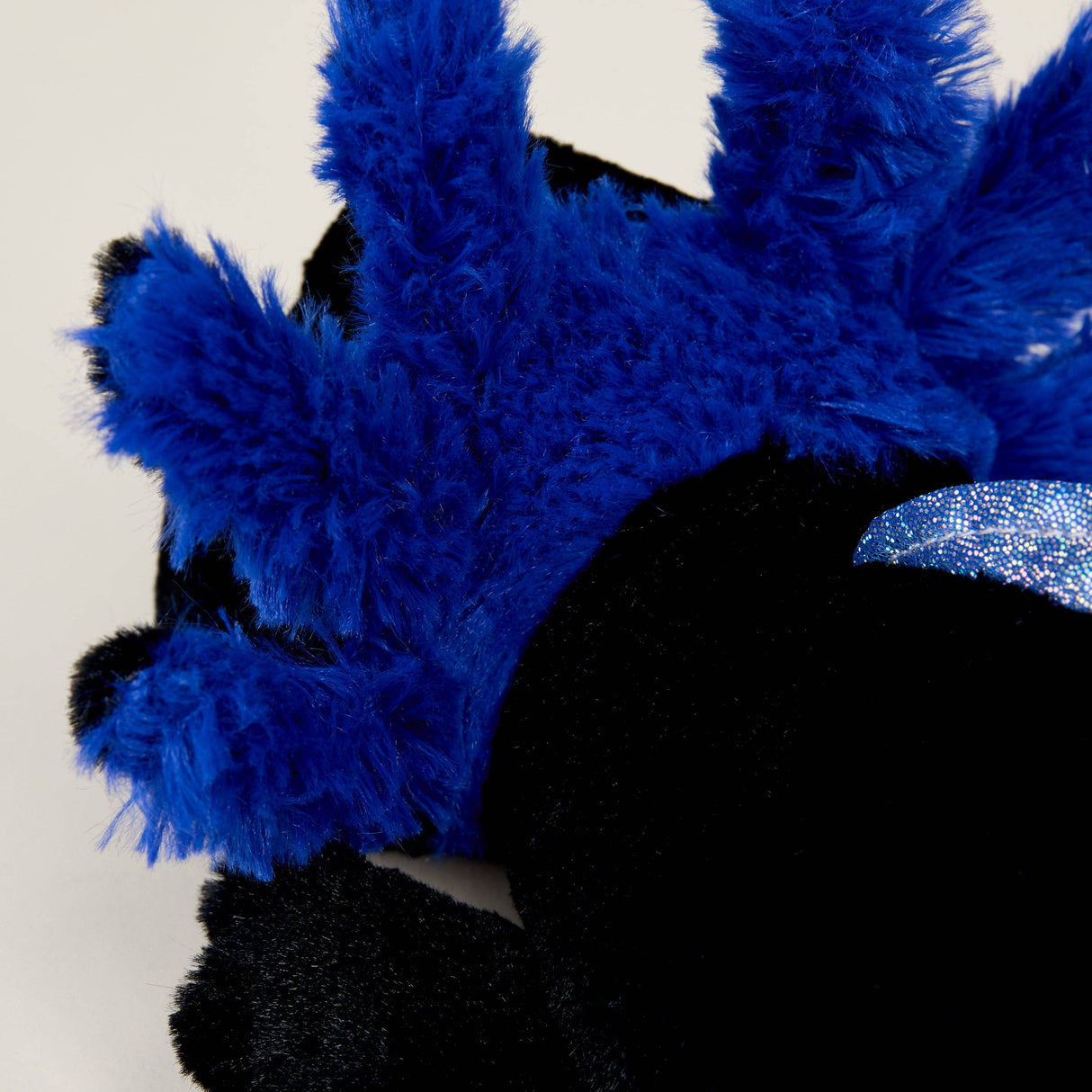 Close-up of a soft plush black axolotl with bright blue fluffy gills and a shiny blue accent on a light background