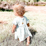 Toddler wearing Natpat | Buzzpatch Mosquito & Insect Repellent Stickers on dress outdoors in grassy area.