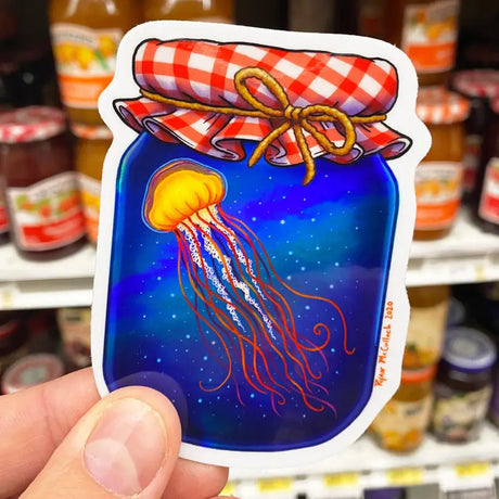 Jellyfish Preserves Holographic Sticker showing vibrant jellyfish in a jar with red checkered lid, art by Ryan McCulloch.