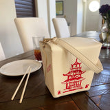 Handbag | Takeout Box shaped crossbody bag with red pagoda design on wooden table next to chopsticks and plate