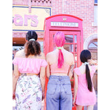 Three women with different hairstyles wearing pastel-colored Honey Bee Hair Scrunchie standing by a red telephone booth.