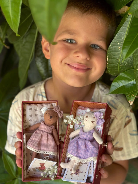 Child holds two fabric bears in stamp boxes, each dressed in lace-trimmed gingham dresses with bows and soft bedding inside