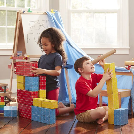 Children playing and building towers with Deluxe Jumbo Cardboard Blocks in bright red, yellow, and blue colors.