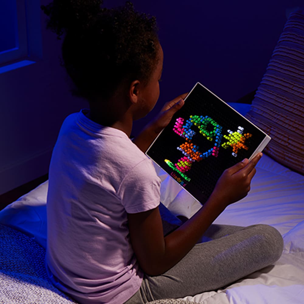 Child playing with colorful illuminated pegs on Lite Brite creating glowing art designs on tablet.