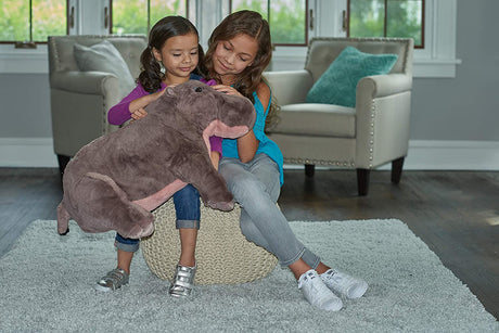 Two girls sitting indoors hugging the Hippo Jumbo large soft stuffed animal plush toy.