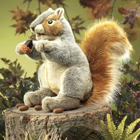 Gray Squirrel Puppet with soft fur, moveable mouth, whiskers, and holding a small acorn, sitting on a tree stump.
