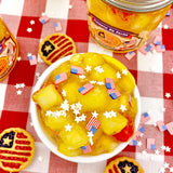 Patriotic Pie Filling Jelly Cube Slime with yellow slime, jelly cubes, star sprinkles, and American flag decorations on a red checkered cloth.