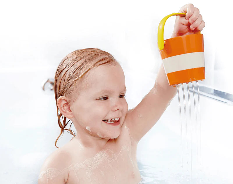 Child playing in bathtub with orange and yellow striped bucket from Happy Buckets Set pouring water with drainage features.