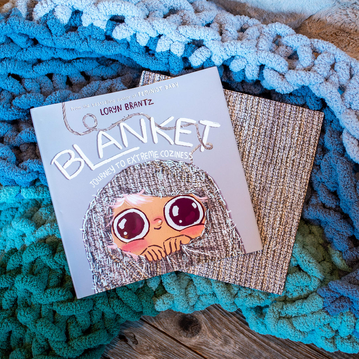 Book titled Blanket Journey to Extreme Coziness resting on a textured blue and beige blanket.