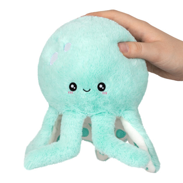 Soft turquoise Octopus Snackers plush toy with eight legs and a smiling face held by a hand.